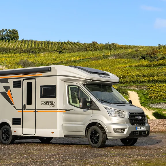 Weißes Forster-Wohnmobil steht vor Weinbergen bei Sonnenschein, Seitenansicht mit markanter Grafik.