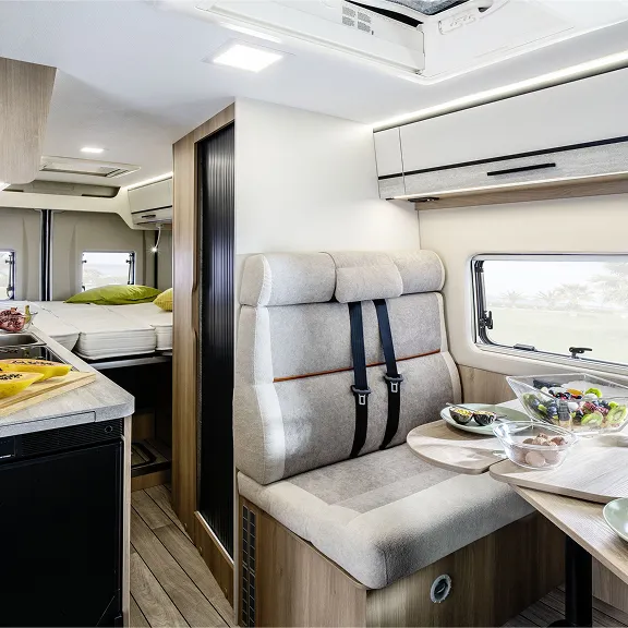 Heller Camper-Innenraum mit Sitzgruppe und Tisch, Küche links und Bett im Heck, gedeckt mit Obst.